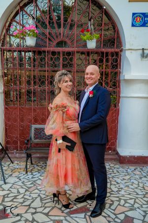 A couple poses together outside a church entrance with decorative red iron gates and stone floor.