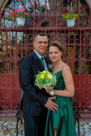 Formal couple embracing in dark green dress and suit by ornate gate.