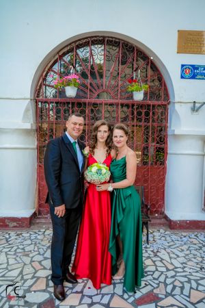 Group photo in formal wear with red and green dresses in front of ornate archway.