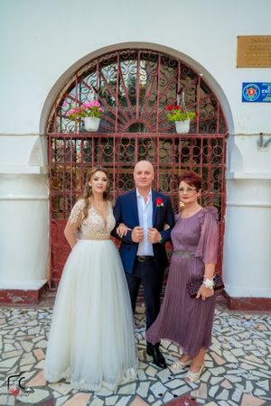 Wedding group photo in front of ornate iron gate with stone paved ground.