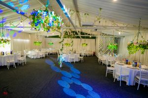 Large white tent wedding reception venue decorated with hanging floral arrangements and blue lighting.