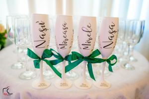 Elegant wine glasses adorned with green ribbons and personalized names arranged on white linen.