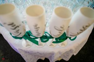 Row of decorated white wine glasses with green ribbons displayed on a white lace tablecloth.