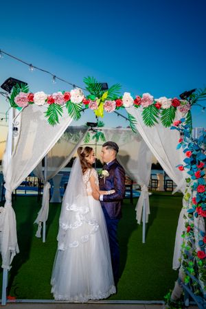 Elegant wedding scene with floral decorations and white fabric draped archway.