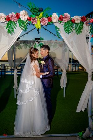 Wedding ceremony setting with pink floral arch and white draping against blue sky.