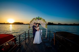 Wedding couple embraces on a boat deck during a stunning sunset over the water.