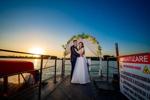 Newlyweds share an intimate moment on a dock during golden hour under a decorated wedding arch.