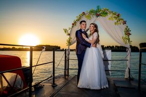 Sunset wedding portrait with floral arch and golden light on waterfront dock.
