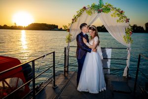 Wedding ceremony setup on dock with white draped arch and sunset reflection on water.