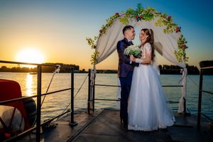 Waterfront wedding scene with decorated arch and golden sunset over lake.