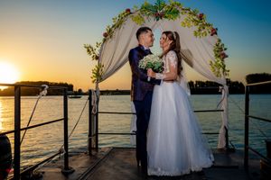 Waterfront wedding ceremony with white floral arch and sunset backdrop.