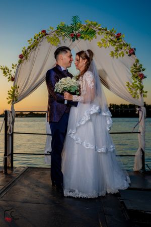 Wedding ceremony at sunset on a dock with floral arch and white draping over water.