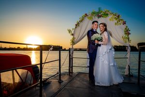 Romantic sunset wedding photo on waterfront dock with decorated arch and golden light.