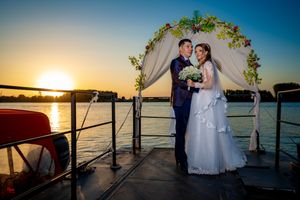 Romantic boat deck wedding portrait with sunset and decorated arch.