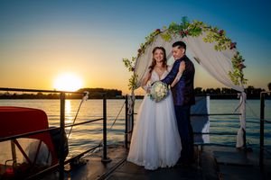 Sunset wedding portrait on boat deck with decorated arch and water backdrop.