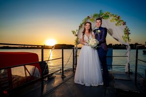Newlyweds stand under a floral arch on a boat deck during golden hour.