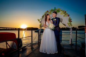 A sunset wedding ceremony on a boat deck with a floral arch overlooking the water.