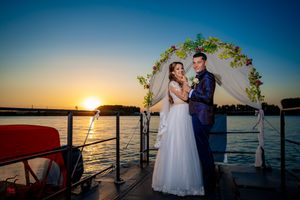 Waterfront wedding celebration with decorated arch against a dramatic sunset backdrop.