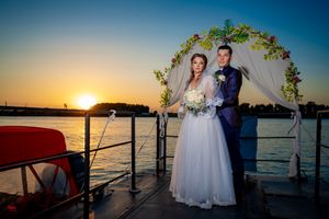 Seaside wedding ceremony setup with floral arch and white draping at golden hour.