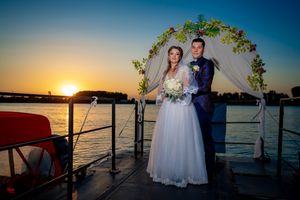 Waterfront wedding ceremony setup with floral arch against a vibrant sunset sky.