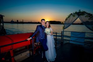 A romantic sunset wedding ceremony on a waterfront deck with floral arch and white draping.