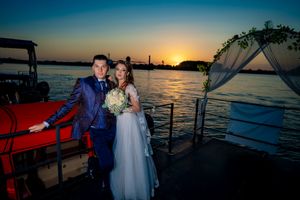 Waterfront wedding ceremony setup with white arch and orange sunset sky.