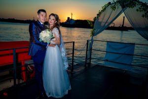 Romantic boat wedding scene with couple against setting sun and calm waters.