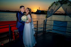 Wedding couple on boat deck with dramatic orange sunset and waterfront backdrop.