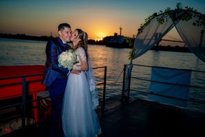 Couple embracing during golden hour on a boat with dramatic sunset silhouettes over the water.