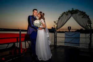 Romantic sunset wedding photoshoot on a boat deck with water and sky in warm golden hues.