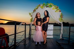 Three people stand together under a decorated arch during golden hour on a waterfront deck.