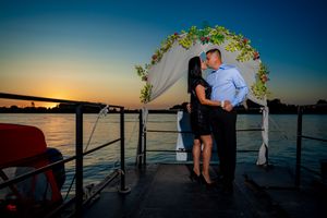 A romantic sunset photoshoot under a decorated arch on a waterfront deck.