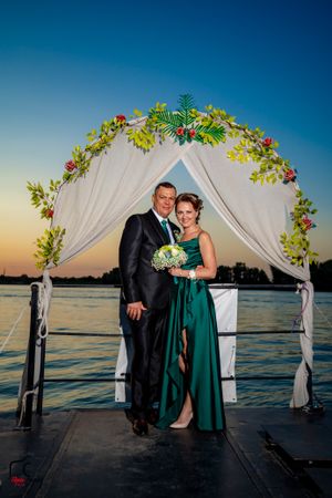 Couple shares romantic moment under decorated wedding arch on lakeside dock.