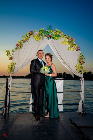 Intimate waterfront wedding ceremony with couple under floral arch at sunset.
