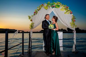 Sunset wedding ceremony on wooden dock with decorated arch and water views.