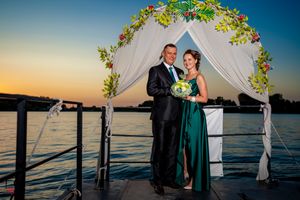 Romantic waterfront wedding ceremony with floral-adorned arch and white draping at dusk.
