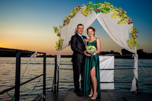 Elegant lakeside wedding arch decorated with greenery and white fabric against blue sky.
