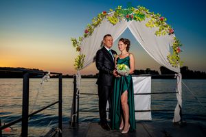 Waterfront wedding ceremony setup with white draped arch and floral decorations at sunset over a lake.