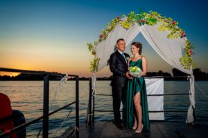 Sunset wedding ceremony setup on a waterfront dock with white fabric and floral arch.
