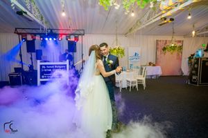 Dramatic fog effects fill the dance floor during a wedding reception with ambient lighting.