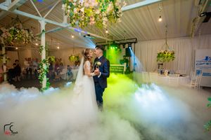 First dance moment captured in a misty venue with dramatic green lighting and hanging floral arrangements.