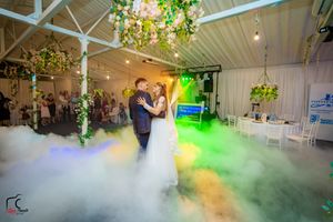 Couple dancing in a dreamy fog-filled reception venue with colorful lighting and floral decorations.