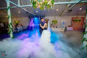 Wedding reception venue with fog-covered floor and vibrant purple and blue lighting effects.