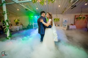 Couple dancing on a fog-covered dance floor with green and blue atmospheric lighting at a wedding reception.