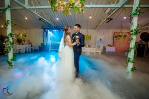 A couple shares their first dance in a beautifully decorated venue with fog effects and colorful lighting.