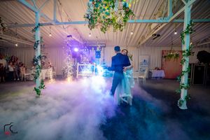 Couple dancing in a dreamy fog-filled reception venue with green vine-decorated pillars and colorful lighting effects.