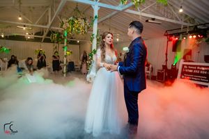 Newlyweds share their first dance on a misty dance floor with colorful lighting and floral decorations.