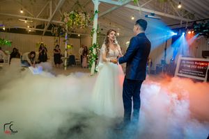 Wedding couple stands amid swirling fog effects with dramatic blue and purple lighting in reception venue.
