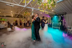 Couples dance surrounded by atmospheric fog effects and colorful lighting at an elegant wedding reception venue.