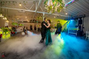 Indoor wedding reception venue illuminated with colorful lighting and atmospheric fog effects.